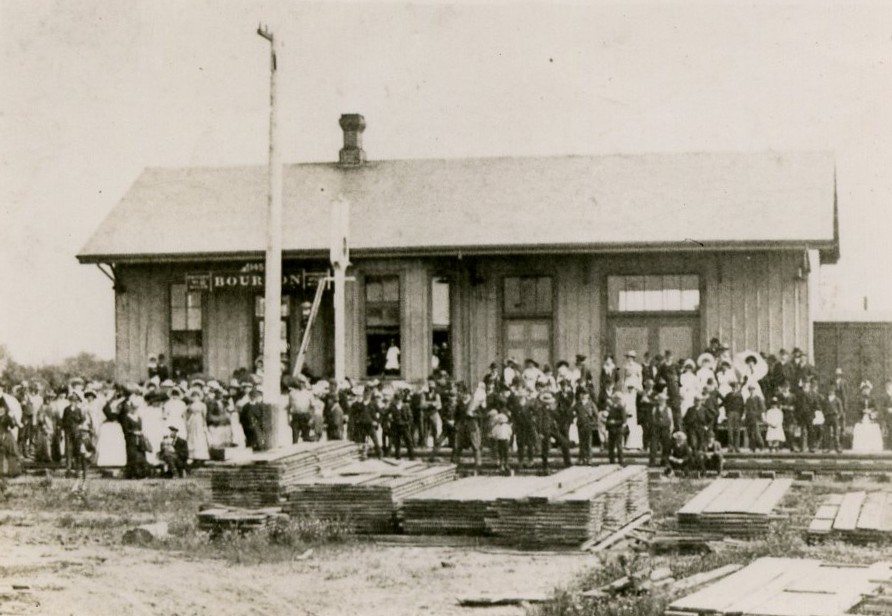 Black and white image of railroad depot with a large crowd of people.