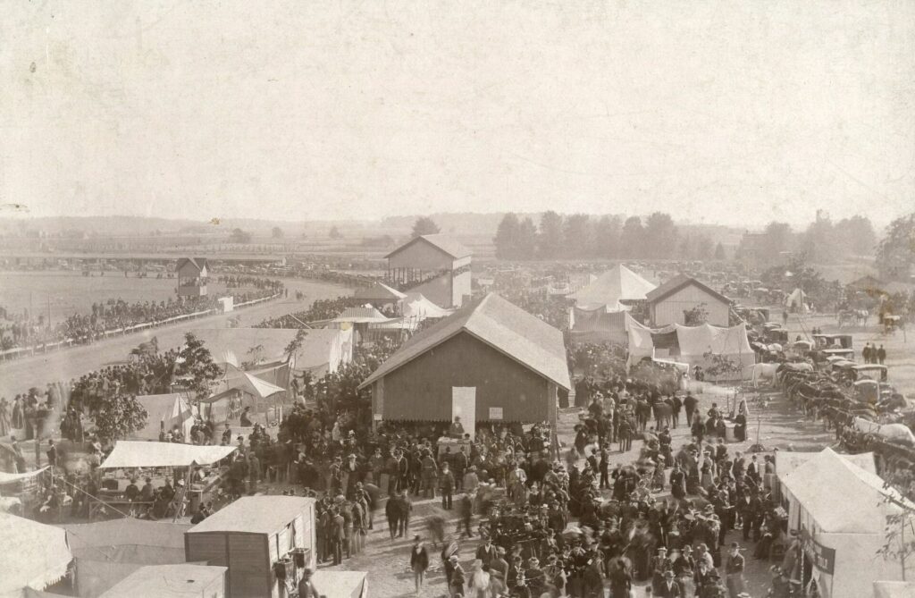Birds eye view of large crowd amongst dirt track and buildings